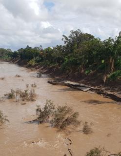 Photo of a flooded river with very brown murky water and damaged concrete along the riverbank