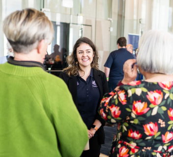 A NEMA employee speaks with two attendees at a conference.