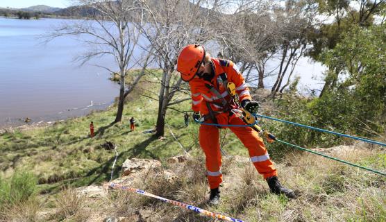 A person in SES uniform rappelling down to a lake.