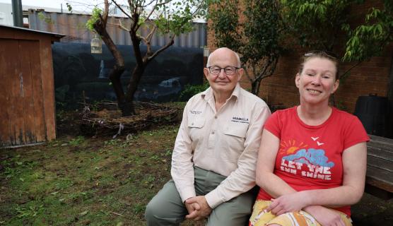Two people sit in a community garden and smile for a photo.