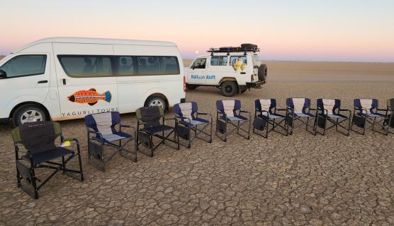 An image of 9 10 camping chairs in front of two vehicles.