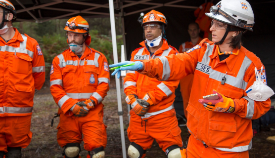 A group of people wearing orange uniforms and hard hats, standing outdoors. They are equipped with personal protective equipment and appear to be a team working together, likely in a field related to engineering or rescue.