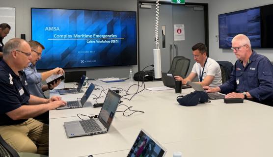 Pup Elliot presenting to Maritime Safety QLD staff seated around a table, with a presentation title slide that says 'Complex Maritime Emergencies'.