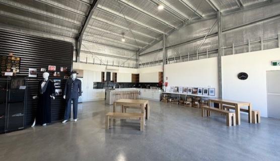 Photo inside the large shed-like facility with polished concrete floors, tables and benches, a kitchenette in the background.