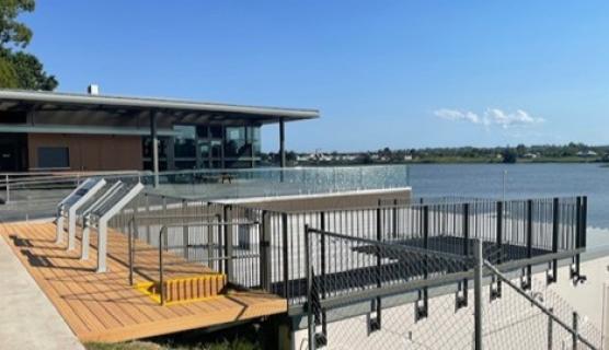 Photo of a building and deck area with railings, overlooking a river with clear blue skies.
