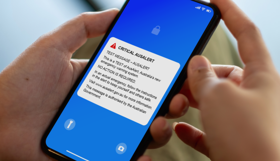 Photo of hands holding a phone with the AusAlert test message on the screen.
