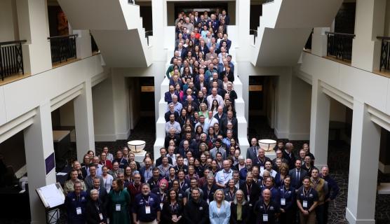 Large group photo of over 150 people on a staircase and spilling out in front of the staircase inside a hotel atrium area.