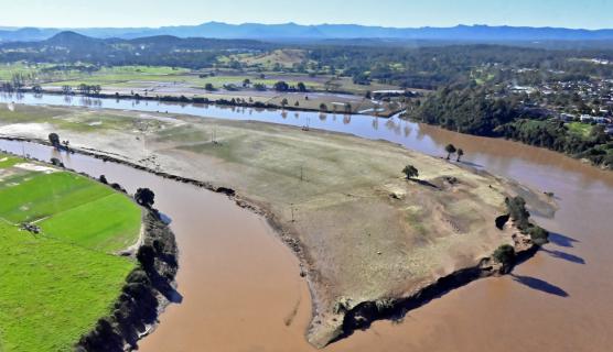 Aerial photo of a very muddy brown river bend with eroded banks but blue sky in the distance.