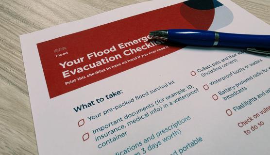 Photo of a piece of paper and pen on a desk. It has a checklist and title 'Your Flood Emergency Evacuation Checklist'.