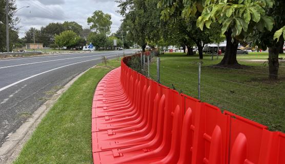 Photo of bright orange plastic flood barriers running along the side of a road and green park.