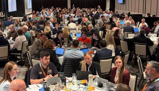 Photo of a large room of about 300 people seated at tables with laptops.