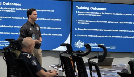 Man presenting in front of slides with 'Training Outcomes' on it.