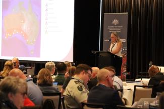 An image of a woman addressing the attendees in front of a lectern at Exercise Convergence 2025