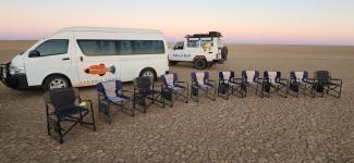 An image of 9 10 camping chairs in front of two vehicles.