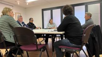A group of 6 people sitting around a white table in an office space.