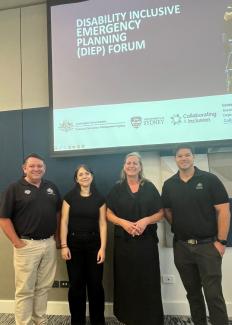 4 people standing underneath a projector with a title slide that says 'Disability Inclusive Emergency Planning (DIEP) Forum.