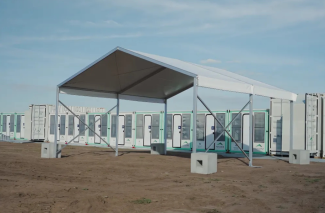Temporary buildings, like containers, lined up on a dirt area with a large barn-like shelter erected in front. 