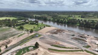 Aerial photo of large construction site by a river with a road running through the middle.