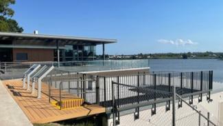Photo of a building and deck area with railings, overlooking a river with clear blue skies.