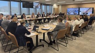 People sitting at desks arranged in a large U-shape with presentation screens at the front of the room.