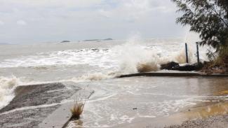 Photo of very rough ocean, grey/brown, hitting a coastal wall.