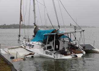 A catamaran/yacht damaged and half submerged in the water, grey skies and rainy weather.