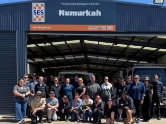 Photo of a large group of people looking at the camera, outside a large shed with SES Numurkah sign above the open roller door.