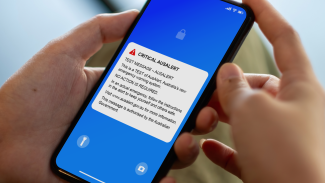 Photo of hands holding a phone with the AusAlert test message on the screen.