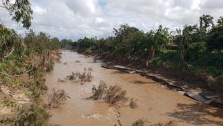 Photo of a flooded river with very brown murky water and damaged concrete along the riverbank