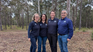 Photo of 4 people wearing NEMA branded shirts, standing in the bush.