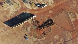 Aerial photo of paddocks, orange-brown ground, and a cattle truck being loaded.