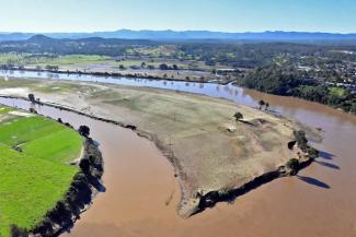Aerial photo of a very muddy brown river bend with eroded banks but blue sky in the distance.