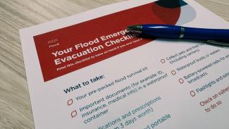 Photo of a piece of paper and pen on a desk. It has a checklist and title 'Your Flood Emergency Evacuation Checklist'.