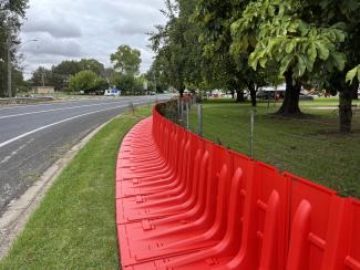 Photo of bright orange plastic flood barriers running along the side of a road and green park.