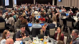 Photo of a large room of about 300 people seated at tables with laptops.
