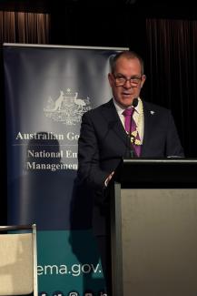 Photo of man in a suit speaking from a lectern with a NEMA banner behind him.
