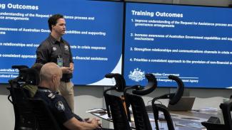 Man presenting in front of slides with 'Training Outcomes' on it.